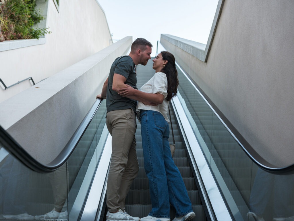 Casal em sessão de pré-casamento, nas escadas rolantes, prestes a dar um beijo. 