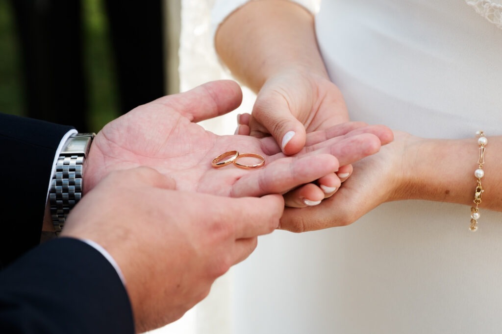 Close-up das alianças de casamento na mão do noivo enquanto a noiva segura nas mãos do amado. 