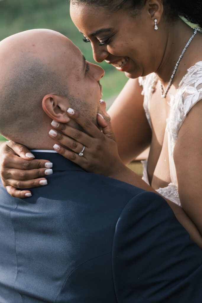Pequena sessão com os noivos durante o casamento, close-up dos noivos sorridentes um para o outro tendo em destaque a aliança da noiva na sua mão encostada à face do noivo. 