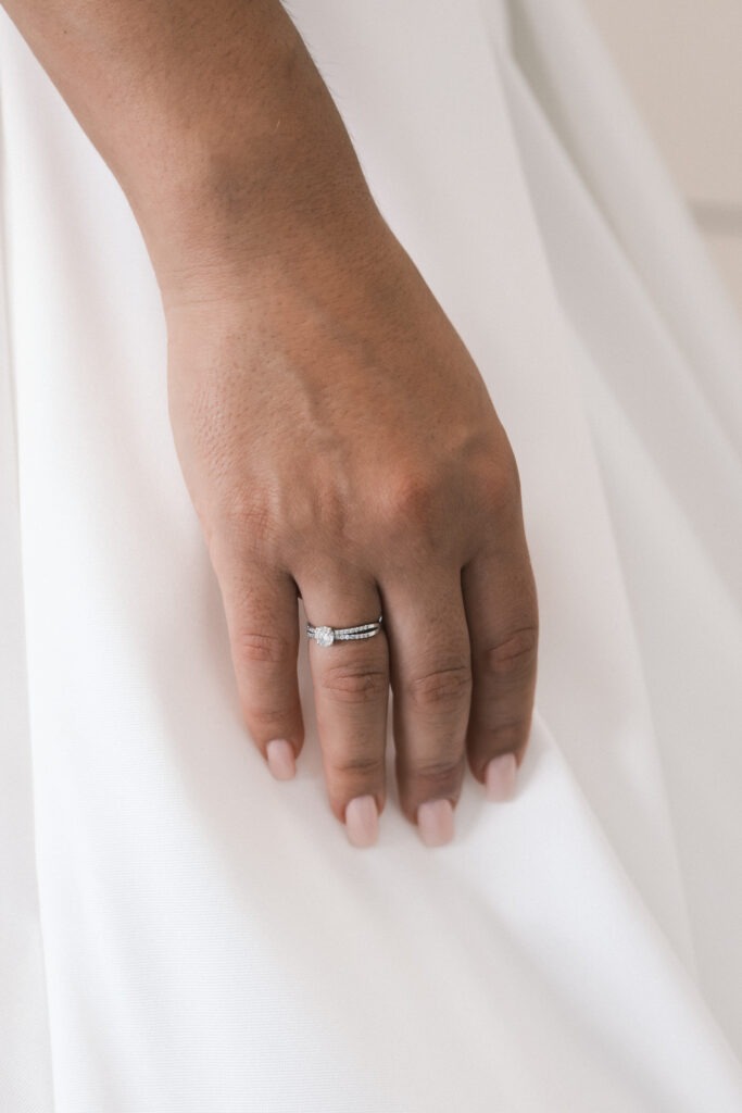 Close-up da mão da noiva com o anel de noivado como foco principal.