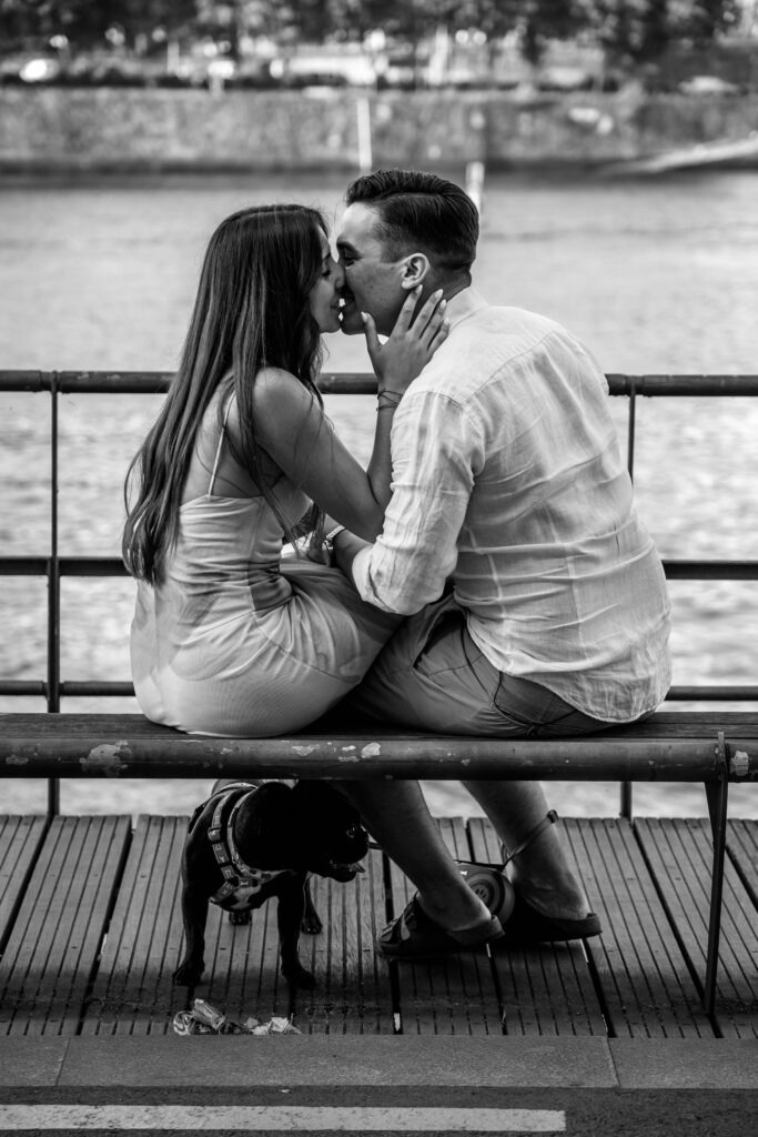 Casal em sessão de pré-casamento, sentados no Cais de Gaia beijando-se alegremente