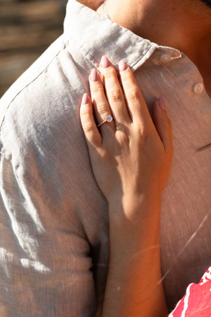 Mão da noiva centrada na imagem com o anel de noivado, estando a mão encostada ao noivo. 