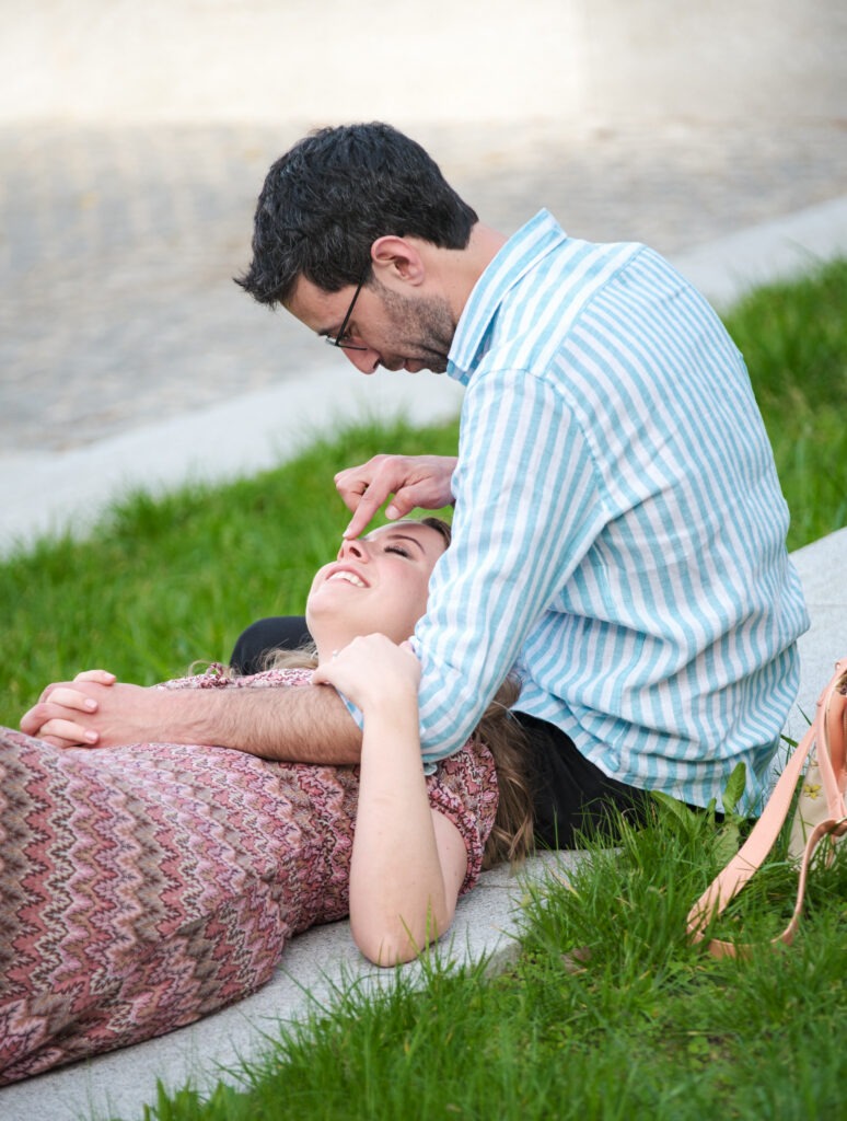  Casal em sessão de pré-casamento num momento divertido, onde a noiva esta deitada no colo do noivo, enquanto este brinca com o nariz da amada. 