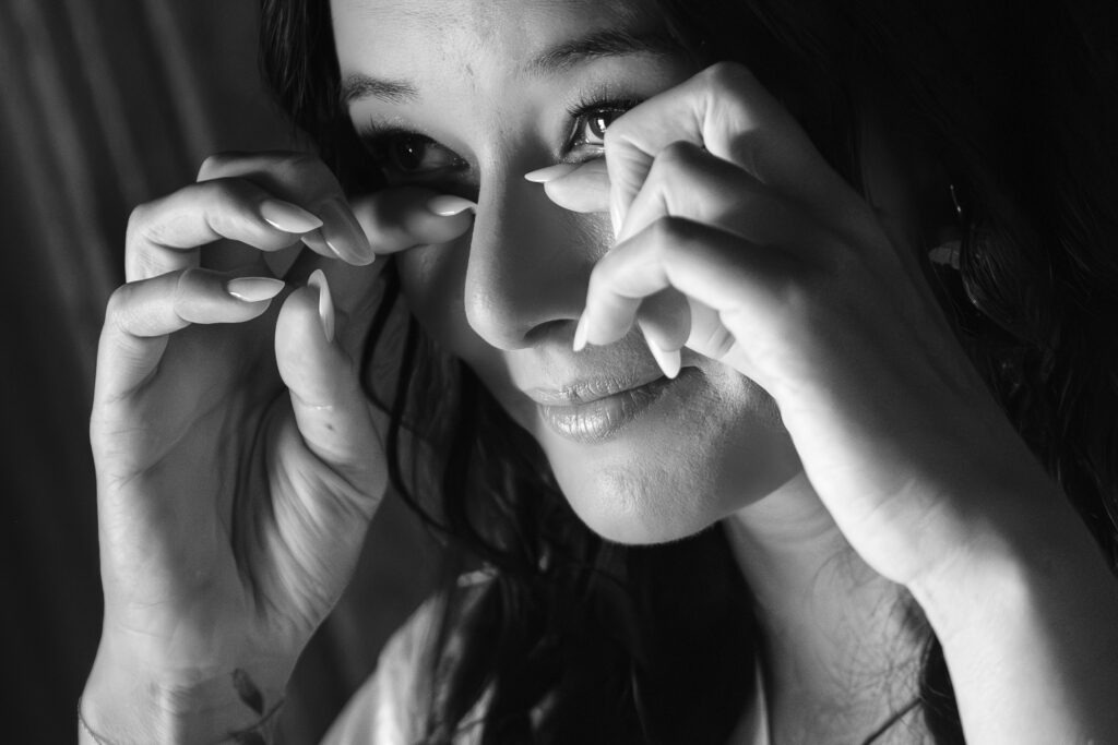 Noiva em close-up a limpar uma lágrima durante os preparativos, luz suave de interior, registo documental no Porto