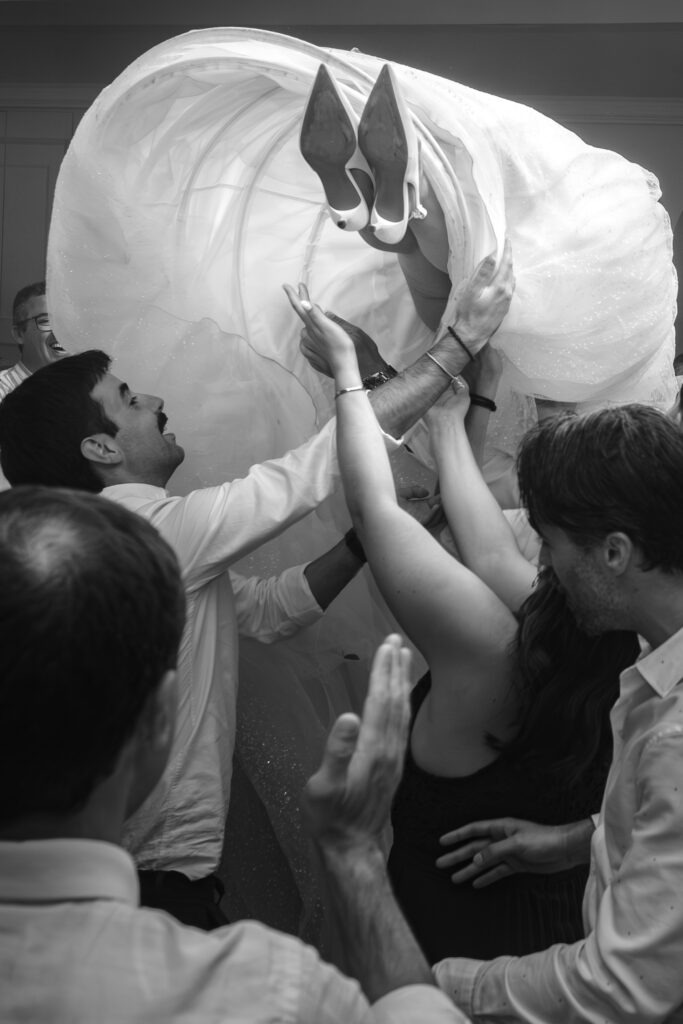 Noiva levantada pelos convidados na pista de dança, vestido em volume e energia de festa, registo documental em Santa Maria da Feira (preto e branco). 