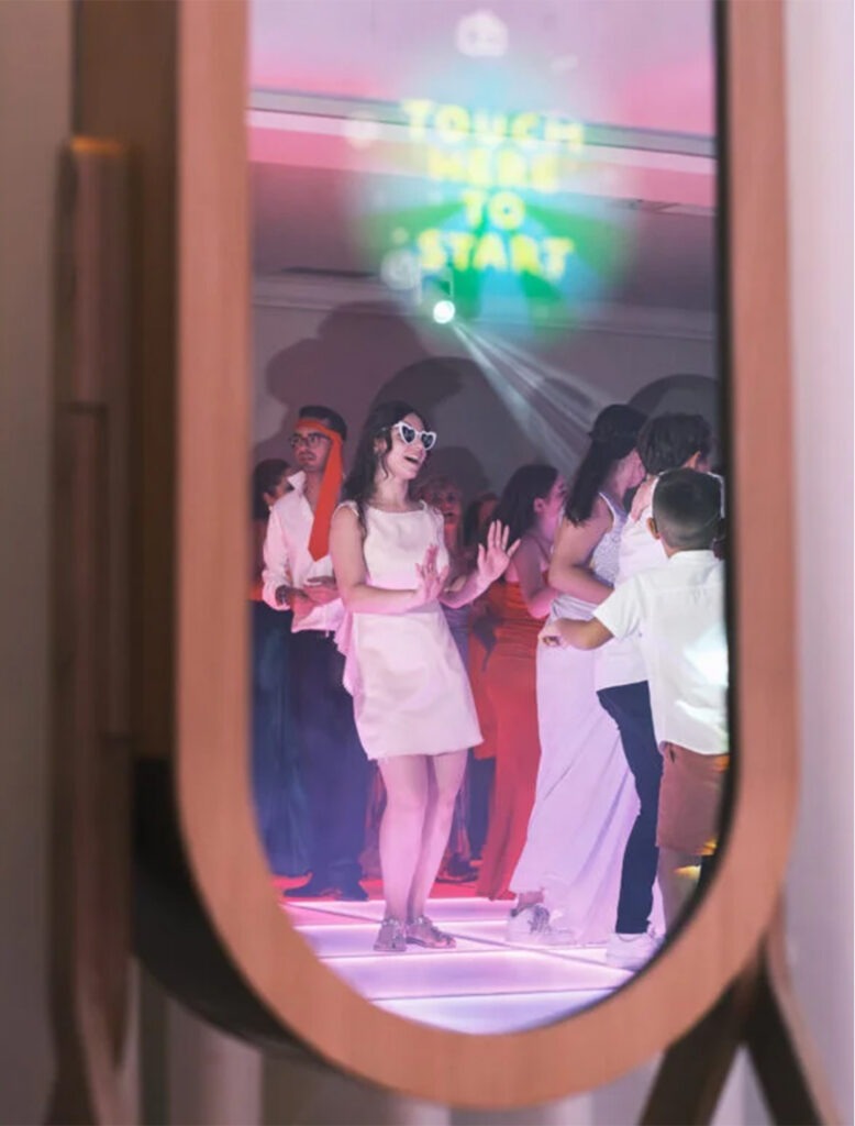 Noiva refletida no espelho do photobooth enquanto dança com os convidados, luzes de festa e ambiente animado em Santa Maria da Feira, registo documental.