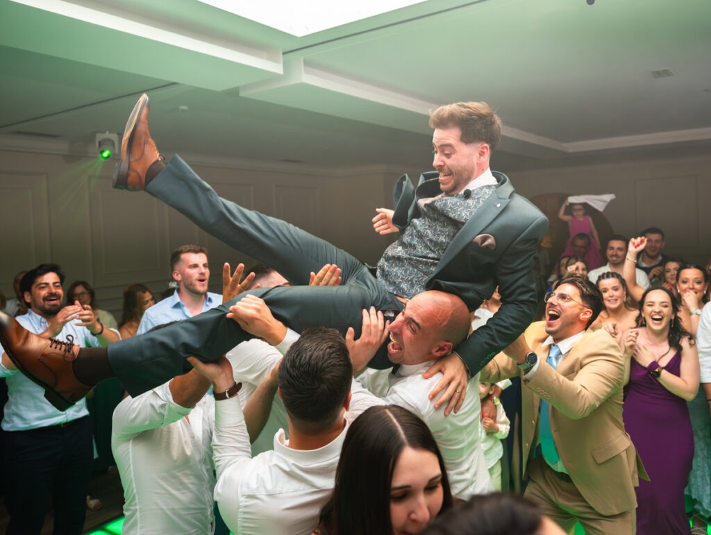 Convidados erguem o noivo e lançam-no ao ar em celebração durante a festa. 