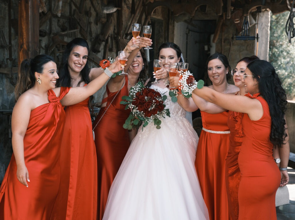 Noiva brinda com as madrinhas do casamento alegremente, as marinhas num tom vermelho a combinar com o ramo da noiva. 