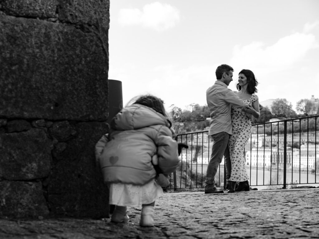 Noivos na sessão de pré-casamento dançando devagar, enquanto a filha em silêncio, atenta a cada movimento dos pais, num registo documental a preto e branco.