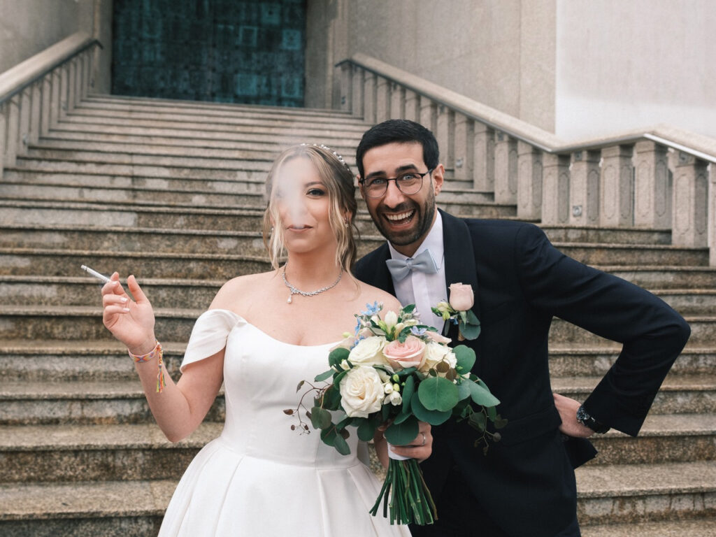 Momento engraçado entre os noivos à saída da igreja, noiva a fumar enquanto o noivo se sorri alegremente para a câmara. 