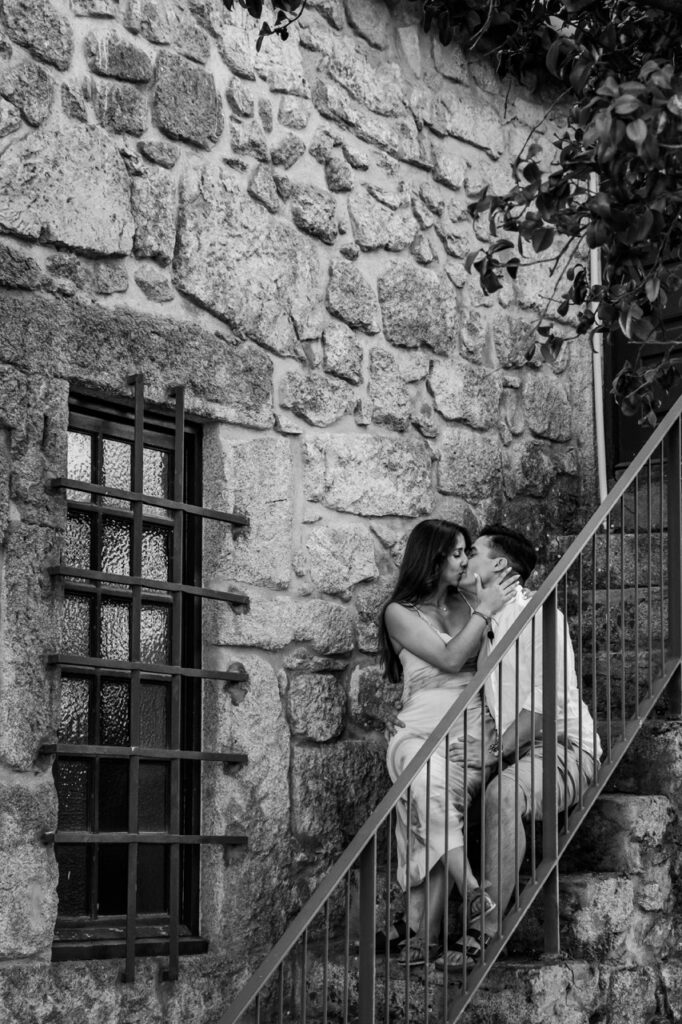 Casal em sessão de pré-casamento, sentados numas escadas, onde a noiva esta sentada no colo do noivo, beijando-se intensamente, registo documental a preto e branco. 