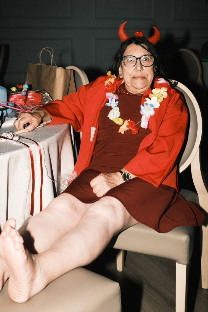 Senhora sentada com os pés descalços noutra cadeira com uma fantasia de diabo na cabeça muito divertida