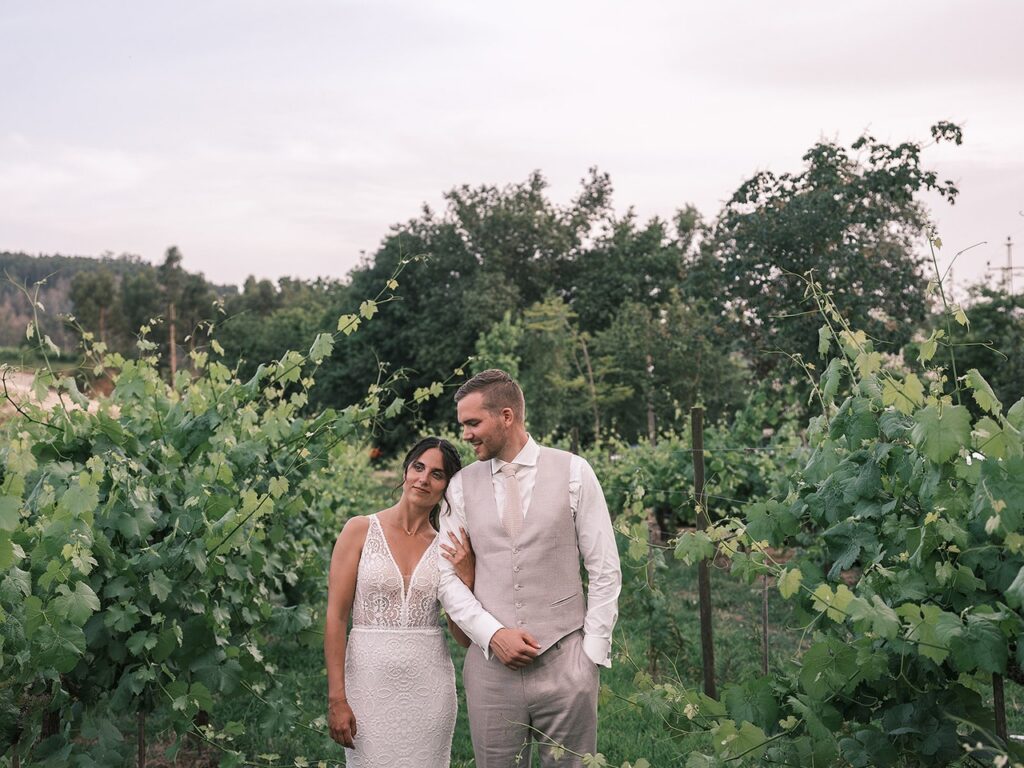 Pequena sessão com os noivos durante o casamento, caminhando entre as videiras, noivo olha para a noiva enquanto esta segura no braço do mesmo 