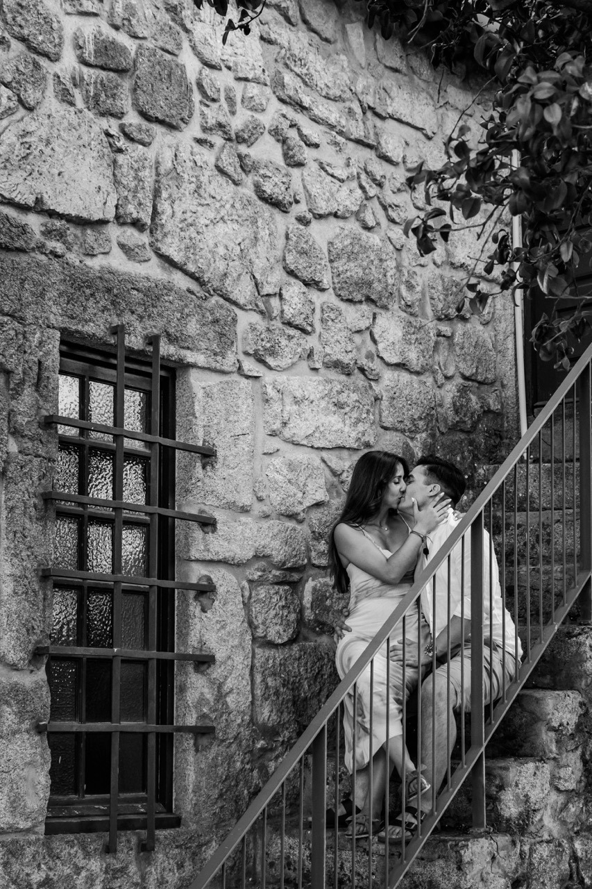 Casal em sessão de pré-casamento, sentados numas escadas, onde a noiva esta sentada no colo do noivo, beijando-se intensamente.