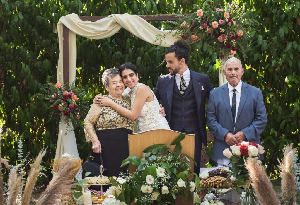 Fotografia tradicional com as pessoas mais chegadas, noiva abraçada a um ente querido enquanto o noivo sorri e a pessoa ao lado tem um olhar frontal para a câmara. 