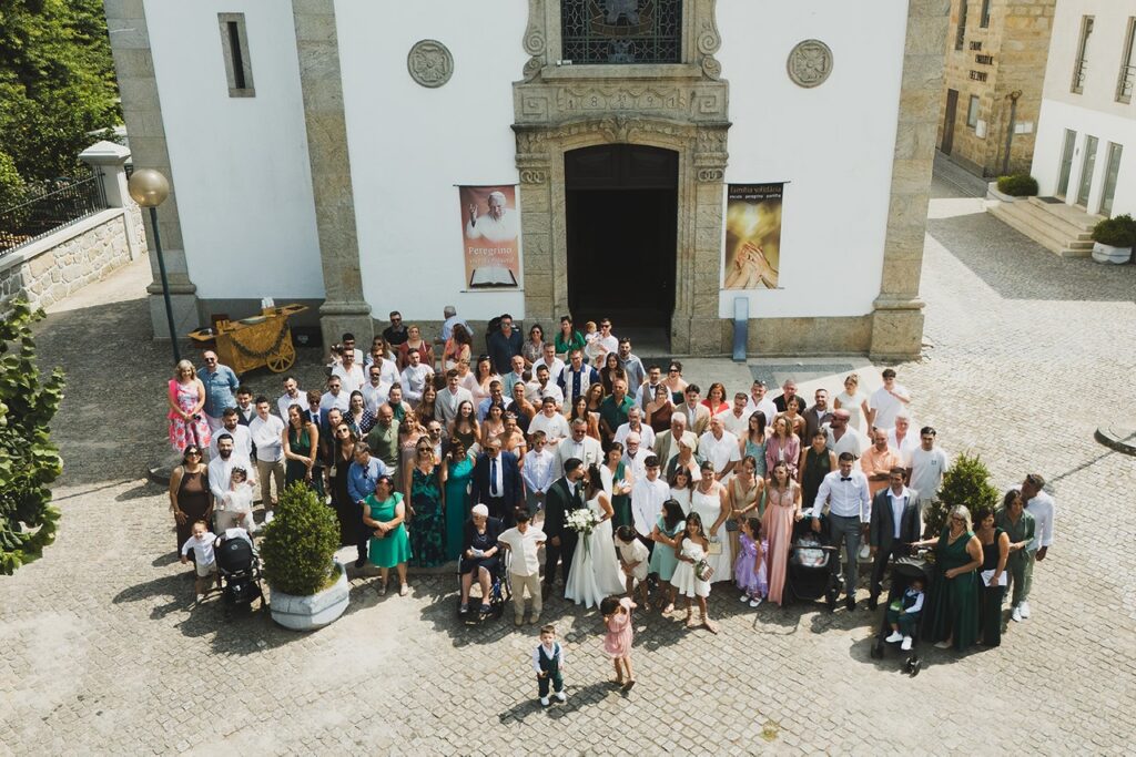 Fotografia aérea do grupo à saída da igreja, com os noivos a beijarem-se. 