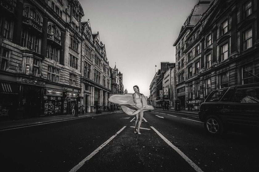 Noiva em vestido de noiva a dançar no meio de rua urbana, elegância e movimento em preto e branco