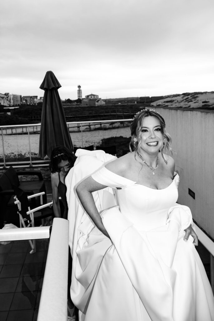 Noiva radiante a segurar a cauda do vestido numa varanda com vista para a ria, registo documental em preto e branco na Quinta do Outeiro, Aveiro.