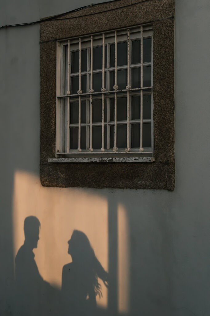 Sombras dos noivos projetadas numa parede com janela, ao pôr do sol no Cais de Gaia, junto ao Douro; momento minimalista e intimista em registo documental.