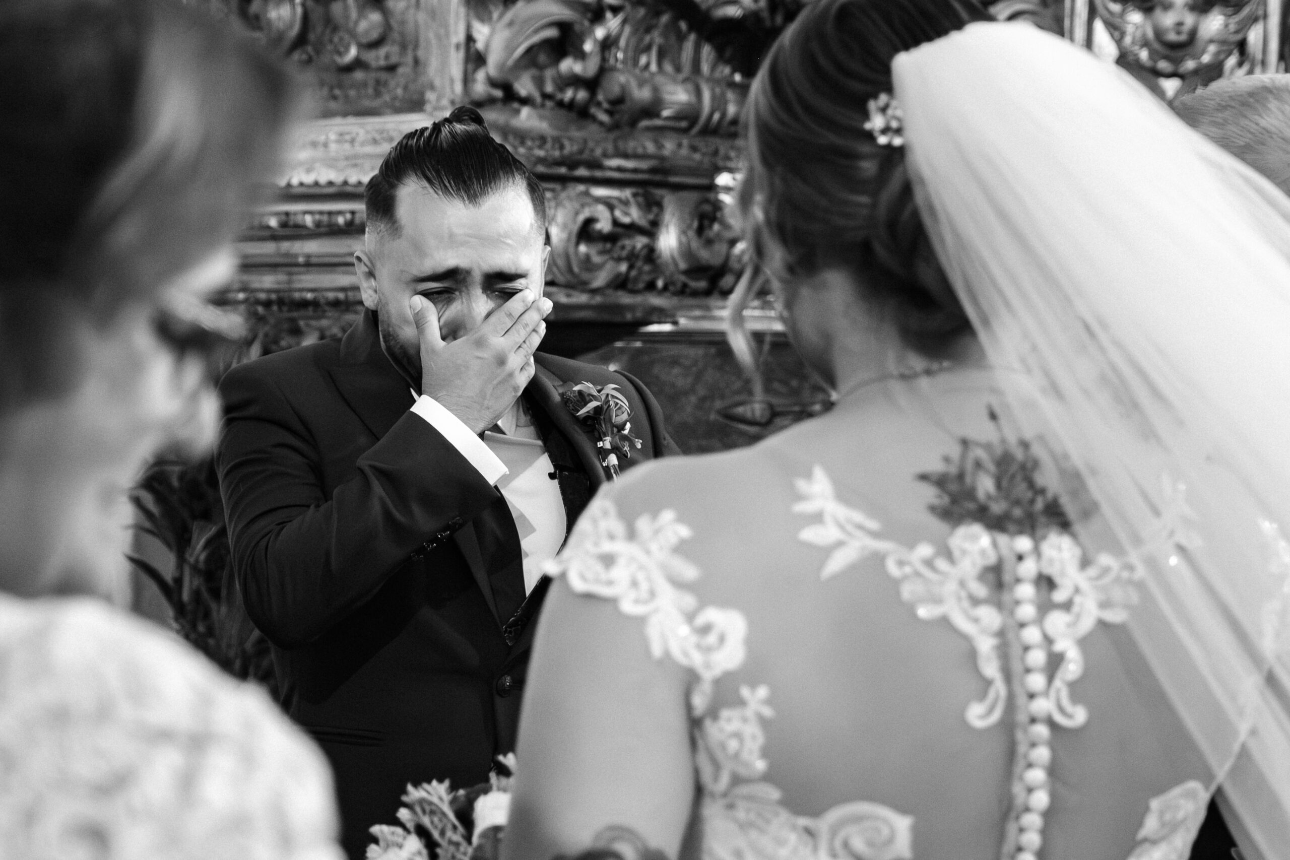 Noivo leva a mão ao rosto, emocionado ao ver a noiva de costas com véu e vestido de renda; interior de igreja, registo documental em Santa Maria da Feira.