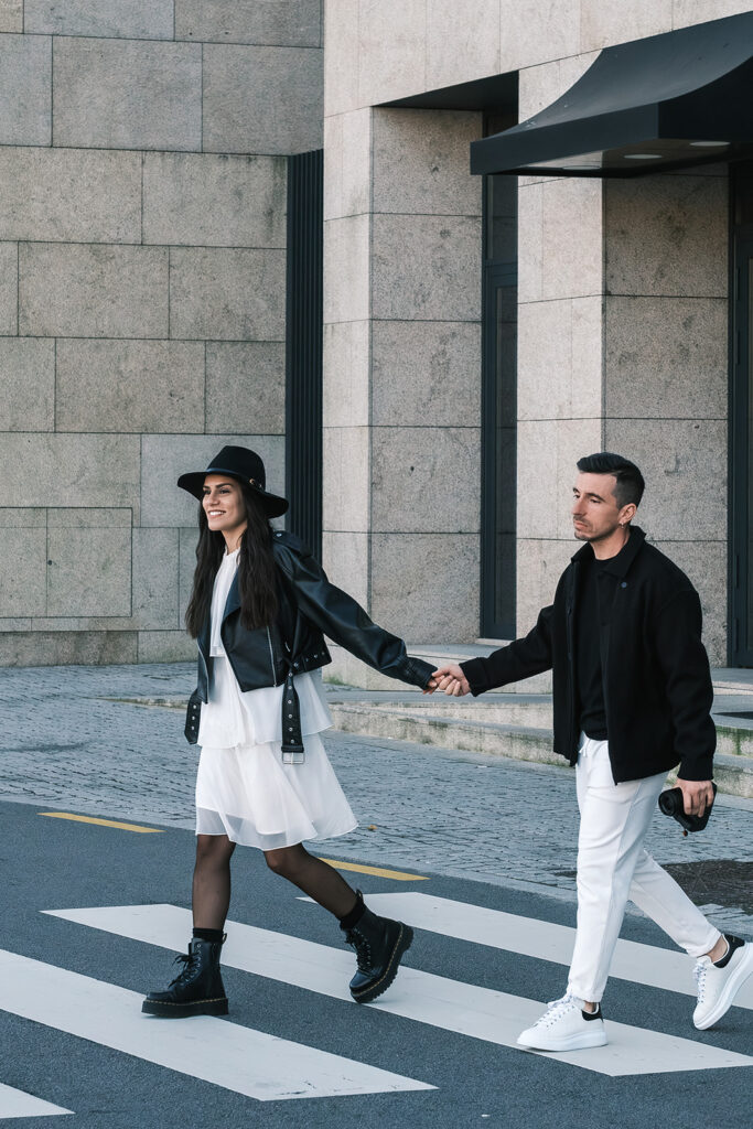 Casal a atravessar rua de mãos dadas em ambiente urbano, sessão pré-casamento Filipe Santos Porto