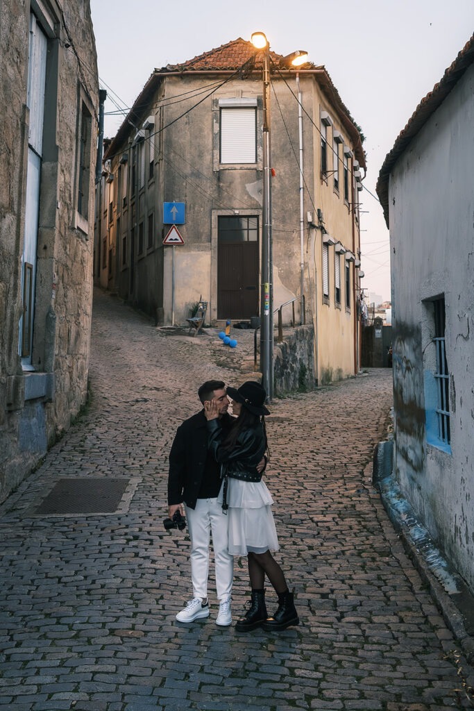 Casal abraçado em rua de paralelepípedos com edifícios antigos ao fundo, sessão pré-casamento Filipe Santos Porto